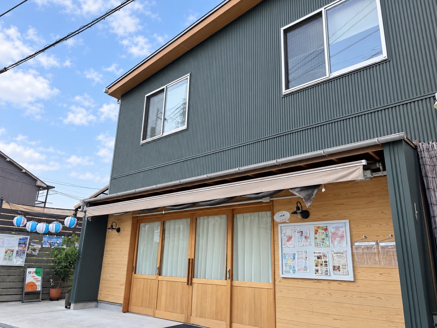 タマリバの外観。緑の壁の2階建てで、1階に木の引き戸と掲示板があります
